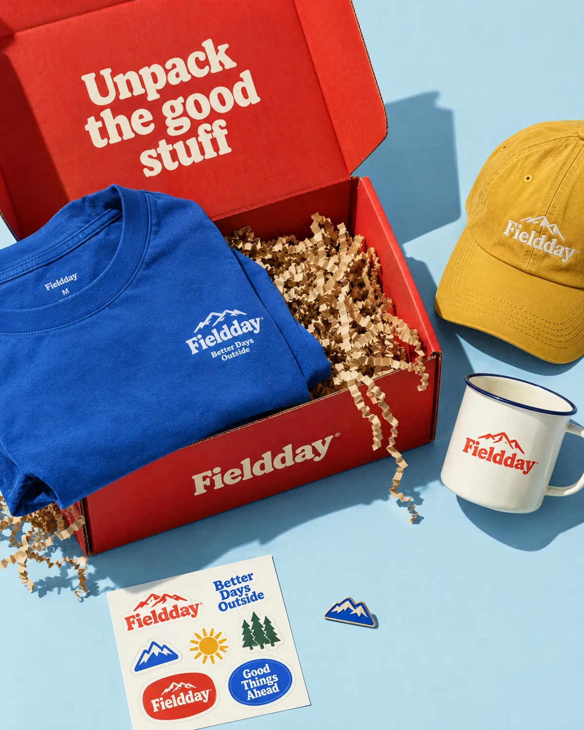 Red Fieldday box with a blue tee, cap, enamel mug and stickers